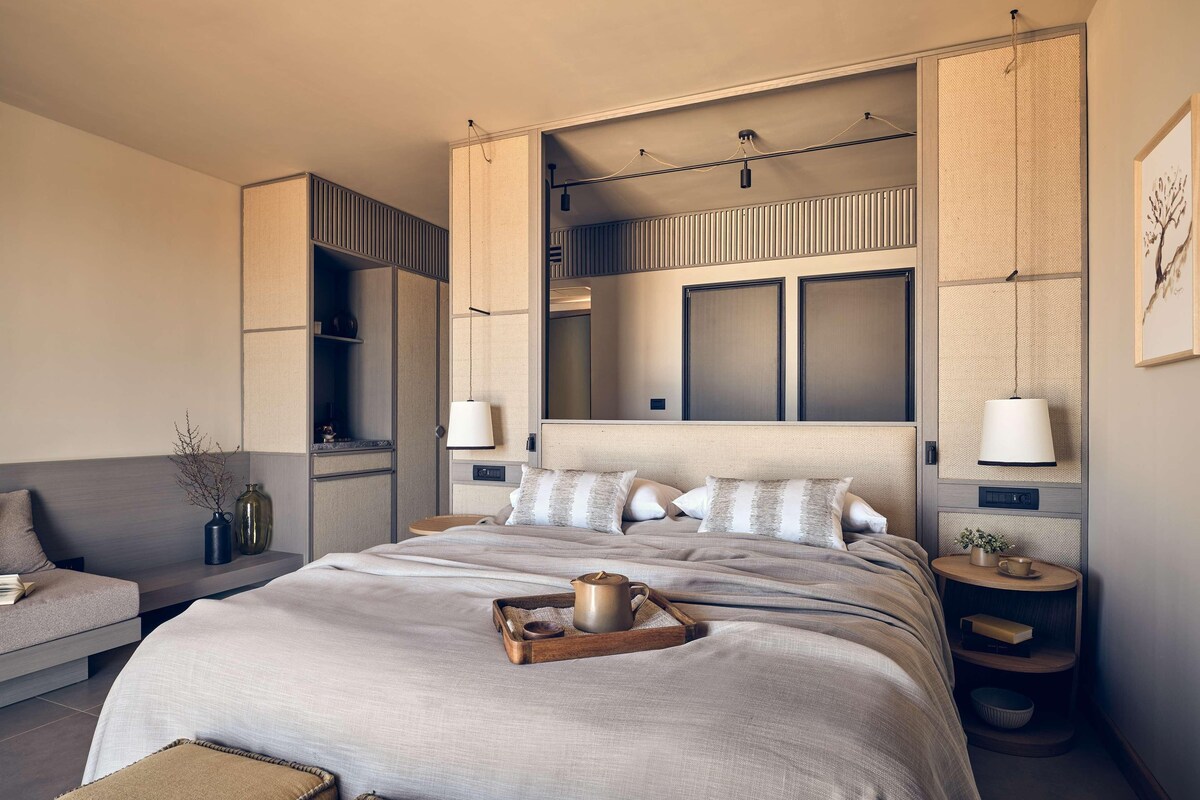 A modern bedroom with a large bed, bedside tables, a built-in wardrobe, and a seating area.