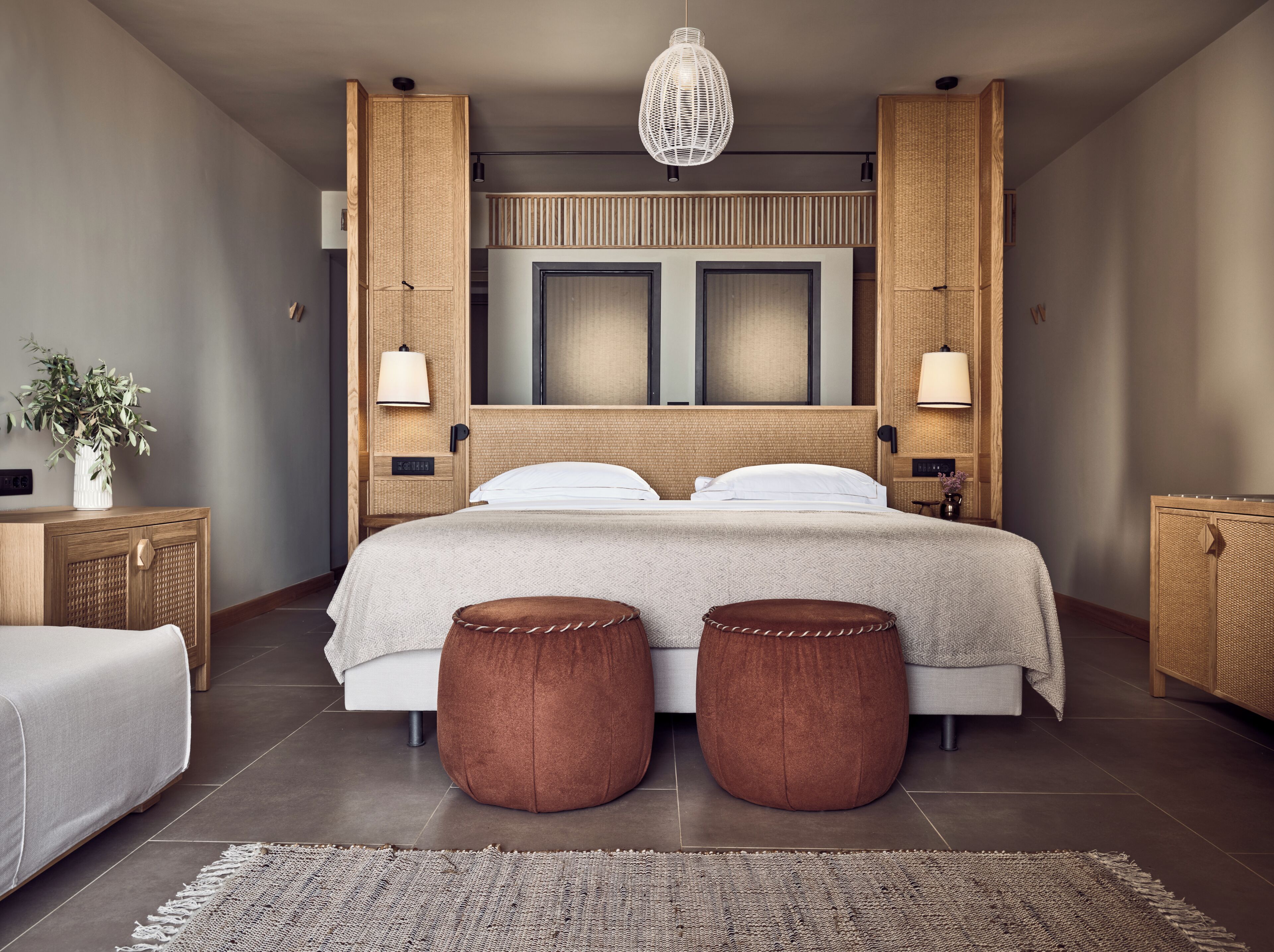 Une chambre moderne avec un grand lit, deux tables de chevet, un luminaire suspendu et une tête de lit en osier.
