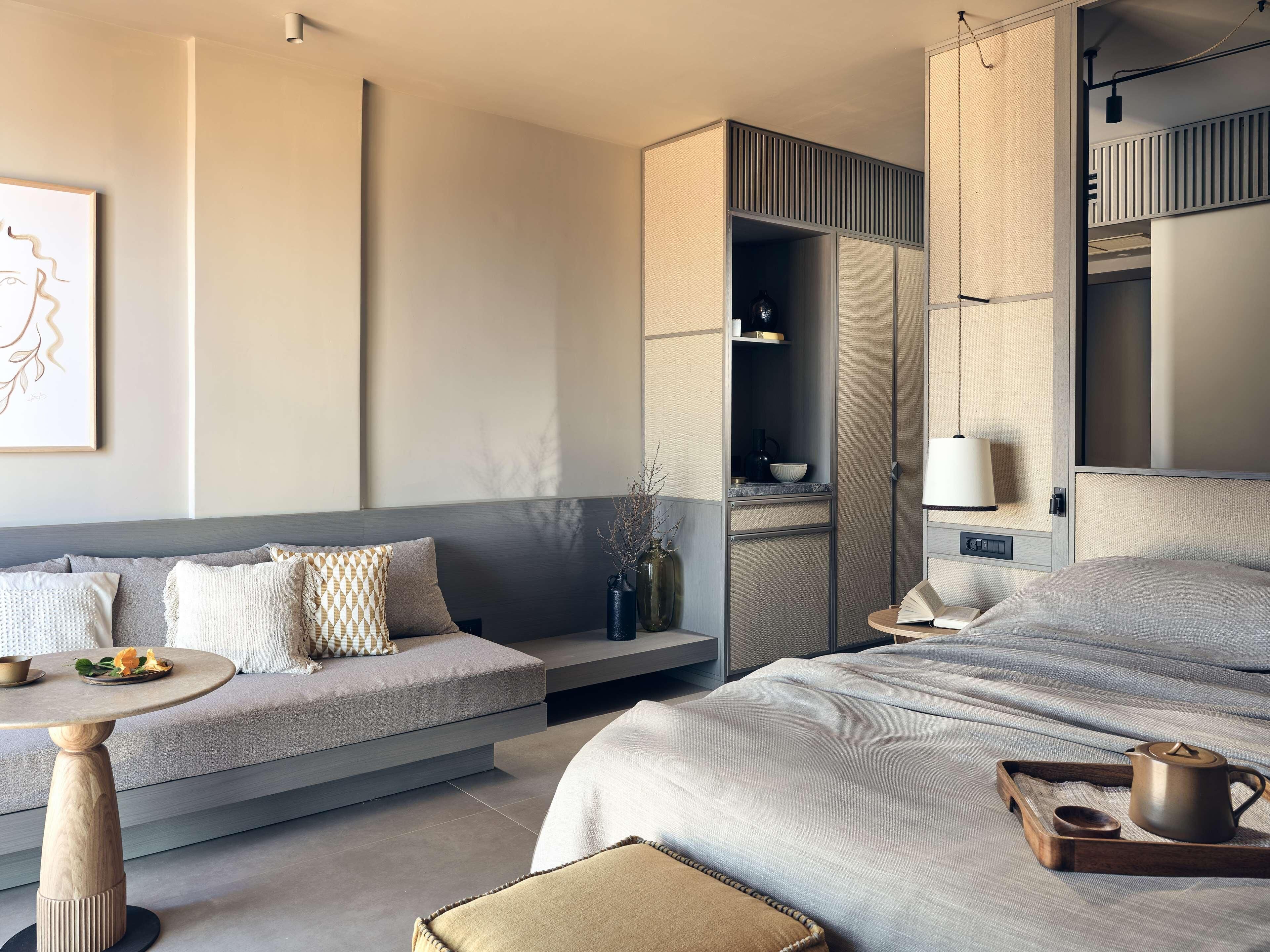 Une chambre d’hôtel moderne équipée d’un canapé, d’un lit, d’une petite table, d’une bibliothèque et d’un luminaire suspendu.