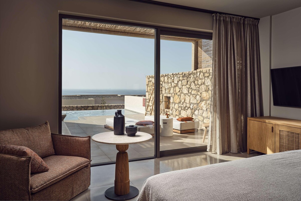 A modern hotel room with a balcony, a bed, a sofa, a small table, and a TV.