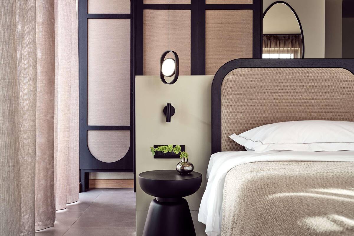 A modern hotel room with a bed, a round mirror, a small side table with a plant, and a decorative wall panel.