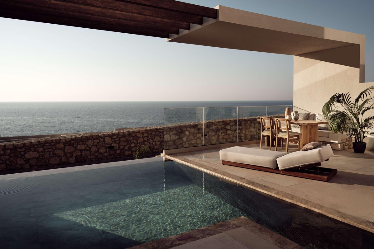 A modern infinity pool with clear water, a stone wall, and a wooden deck.