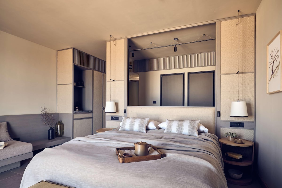A modern hotel room with a large bed, bedside tables, a sofa, and a built-in wardrobe.