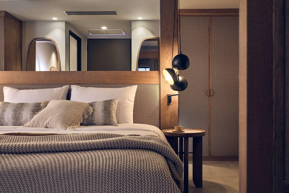 A modern bedroom with a wooden headboard, a round bedside table with a lamp, and a patterned wall.