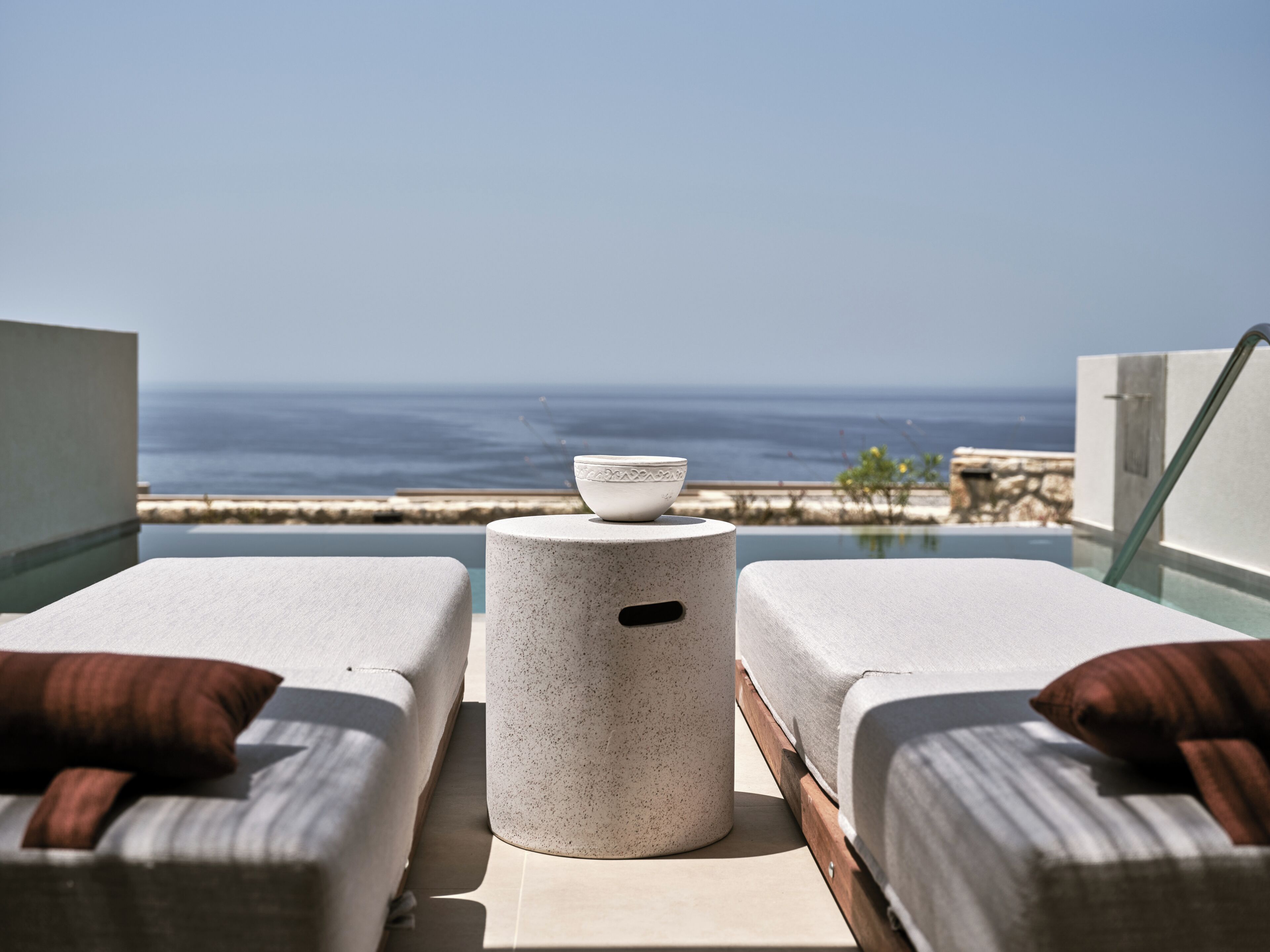 Un balcon avec deux fauteuils de jardin, une petite table ronde et un saladier. La vue comprend l’océan et une côte lointaine.