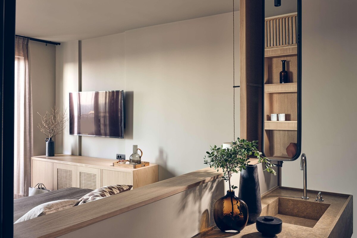 A modern bedroom with a bed, bedside table, a large mirror, a TV, and a wooden shelf unit.