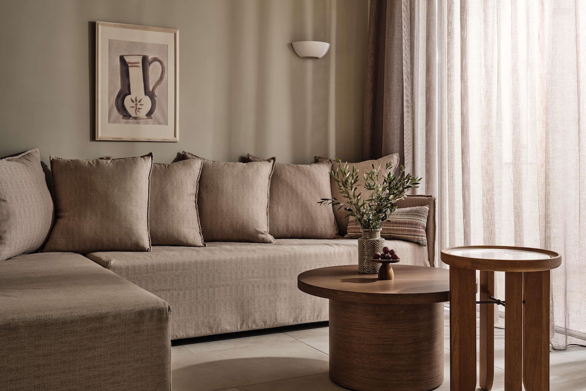 A living room with a sofa, a round wooden coffee table, and a vase with plants.