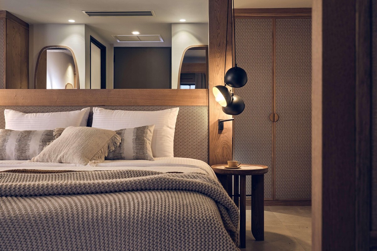 A modern bedroom with a wooden headboard, a round bedside table with a lamp, and a patterned wall.