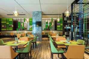 A modern restaurant with green and orange seating, a central pillar, and a wall-mounted TV. - Hampton APT Hilton Hangzhou Olympic (HANGZHOU)