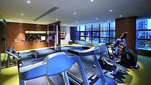 A modern gym with cardio equipment, a seating area, and large windows offering a city view. - Hampton By Hilton Qujing (Qujing)
