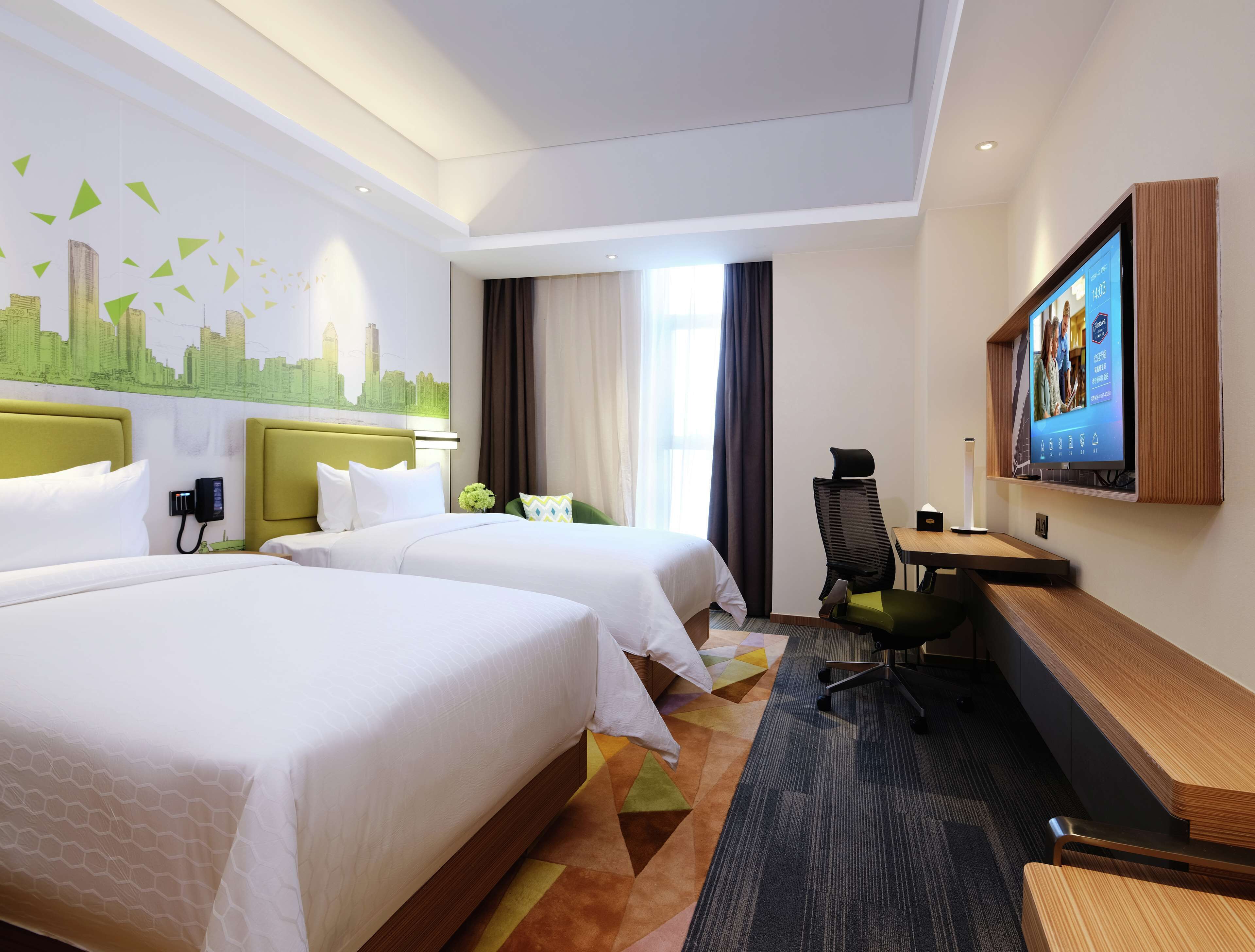 Ein Hotelzimmer mit zwei Betten, einem Schreibtisch, einem Stuhl, einem Fernseher und einem Stadtbild-Wandgemälde.