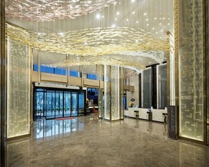 Un lobby amplio con techo alto, piso reflectante y decoración moderna.