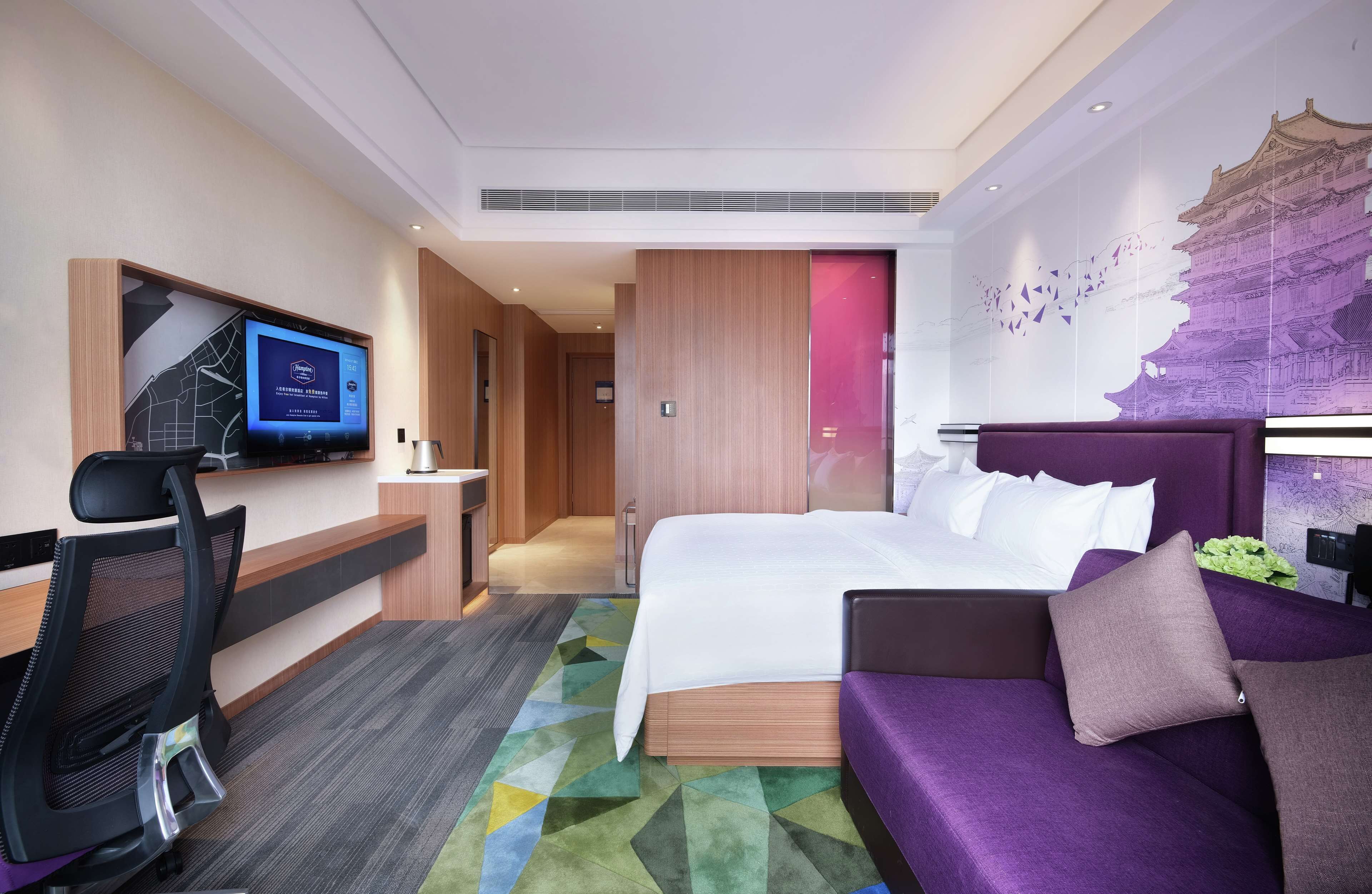 A hotel room with a bed, a desk, a chair, and a television.