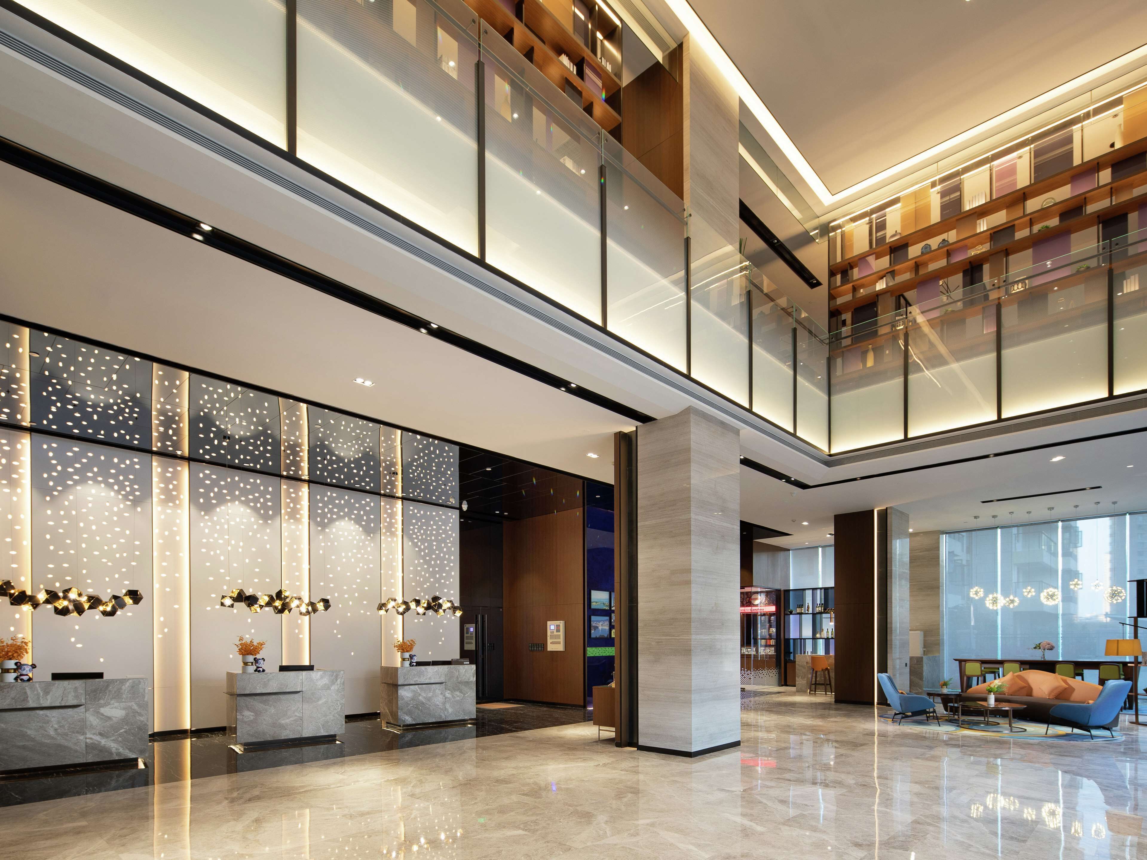A spacious lobby with a high ceiling, a reception desk, seating area, and a staircase leading to an upper level.