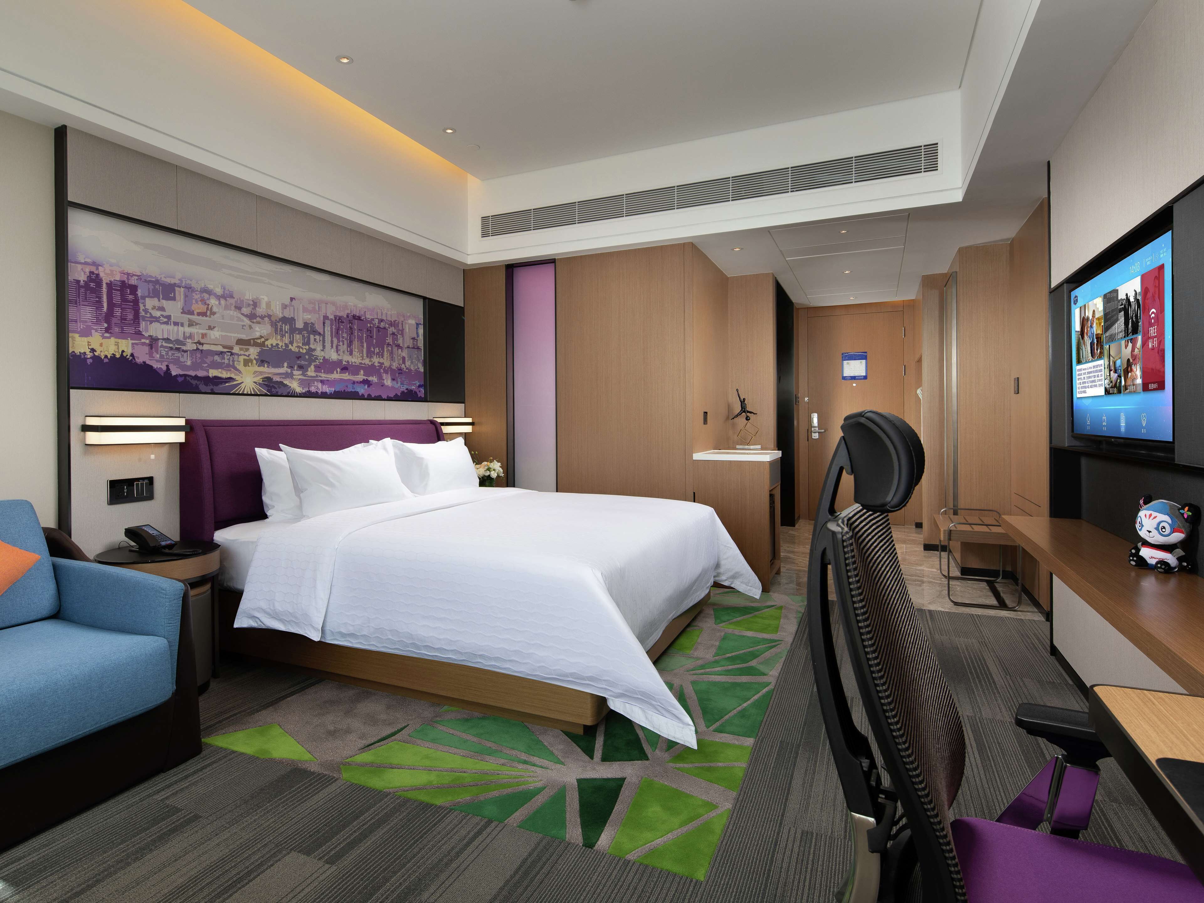 Una habitación de hotel moderna con una cama grande, un escritorio, una silla, un televisor y un cuadro de un paisaje urbano en la pared.