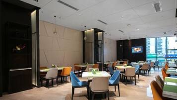 A modern dining area with tables and chairs, a television screen, and a view of the city.