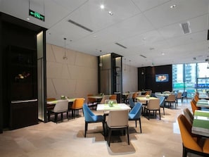 A modern dining area with tables and chairs, a television screen, and a view of the city.