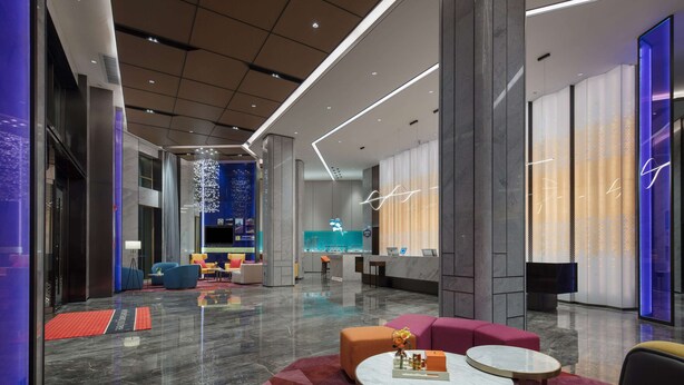 Um lobby moderno com balcão de recepção, áreas de estar e uma instalação de iluminação decorativa.