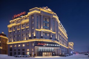 Ein großes, mehrgeschossiges Hotel mit einem auffälligen 'Hampton'-Schild, das einen klassischen Baustil mit symmetrischen Fenstern und einem zentralen Eingang aufweist.