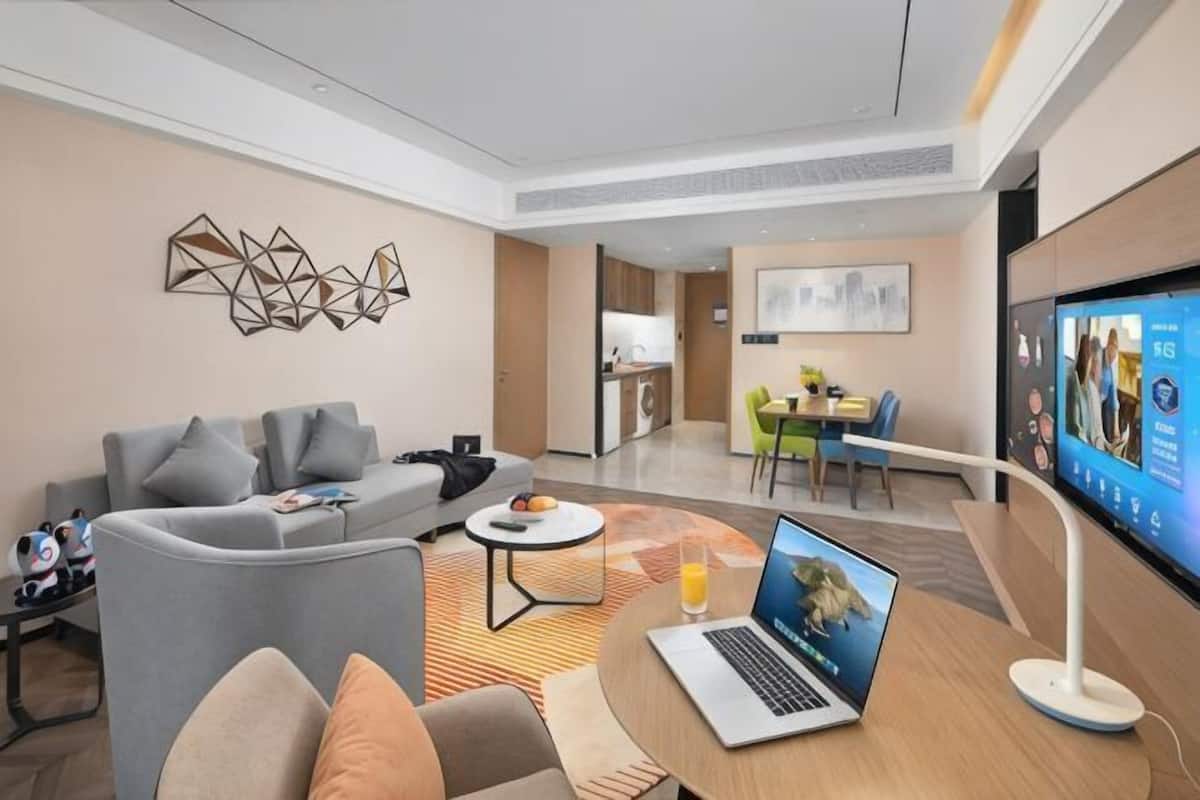 A modern hotel room with a sofa, a coffee table, a laptop, and a TV.
