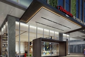 En moderne hotelindgang med en glasfacade, et tydeligt skilt og et reception område.