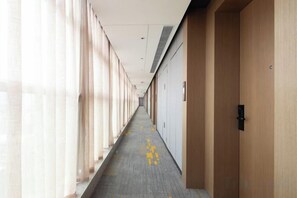 A corridor with a carpeted floor, doors on the right, and windows on the left. - Hampton Apartments by Hilton Shenzhen Futian Mangrove Park (Shenzhen)