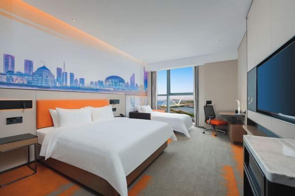 A hotel room with two beds, a desk, a chair, and a large TV.