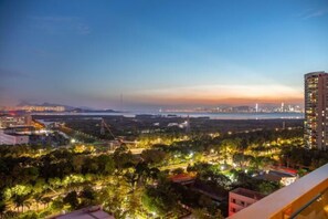 Une vue d’une ville au crépuscule, avec des bâtiments illuminés, un pont et une étendue d’eau en arrière-plan.