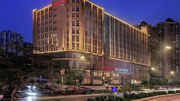 A multi-story hotel with a prominent 'Hampton' sign, large windows, and a well-lit facade.