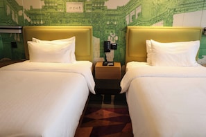 A hotel room with two beds, each with a headboard and white bedding. There is a nightstand between the beds with a clock and a small table. The walls have a green patterned wallpaper.