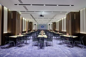 A conference room with multiple tables and chairs, a projector screen, and a logo on the back wall.
