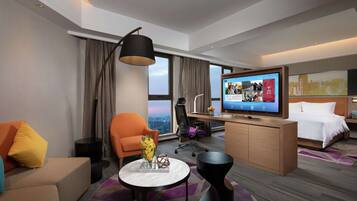 A modern hotel room with a sofa, armchair, desk, and bed.