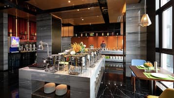 A modern hotel lobby with a marble reception desk, a buffet area, and a seating area with a view of the city.