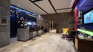 En modern hotellobby med marmorgolv, en receptionsdisk, en bardel, sittplatser och en tv-skärm som visar en karta.