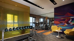 Ett gym med träningsutrustning, en bänk, hantlar, ett löpband och en stol med en vas med blommor.