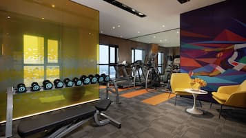 A gym with exercise equipment, a bench, dumbbells, a treadmill, and a chair with a vase of flowers.