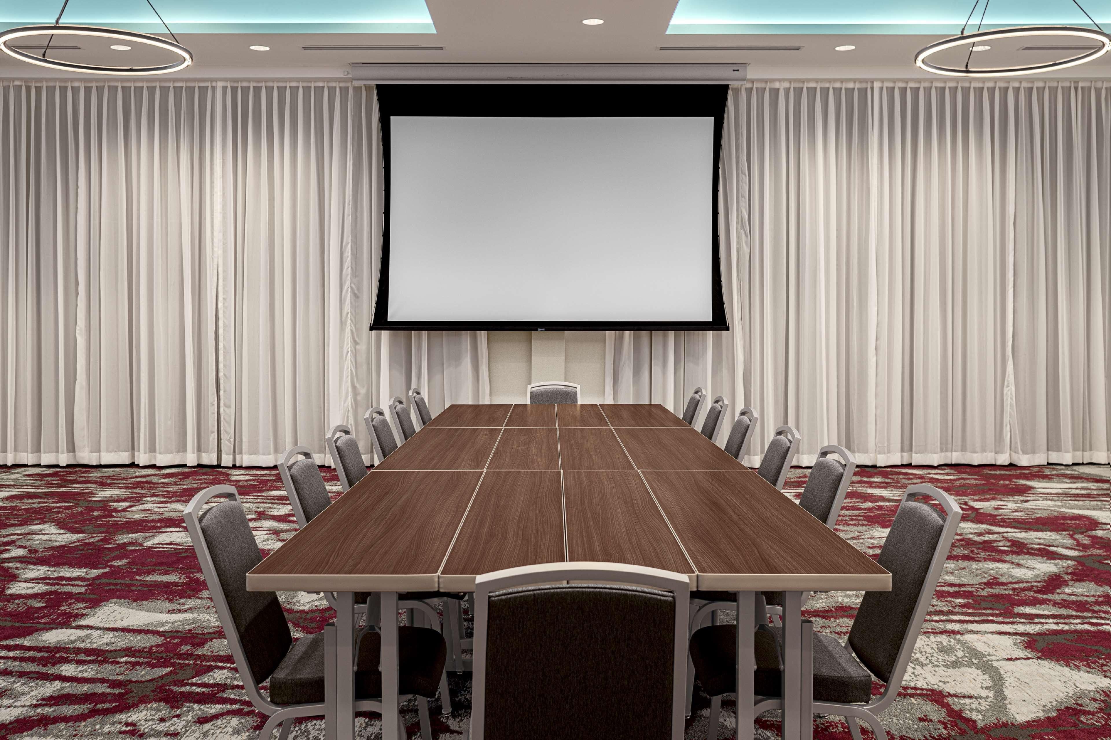 A conference room with a large table, chairs, a screen, and curtains.