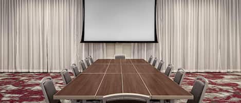 A conference room with a large table, chairs, a screen, and curtains.