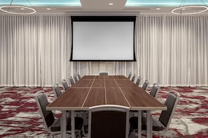 Una sala de conferencias con una gran mesa, sillas, una pantalla y cortinas.