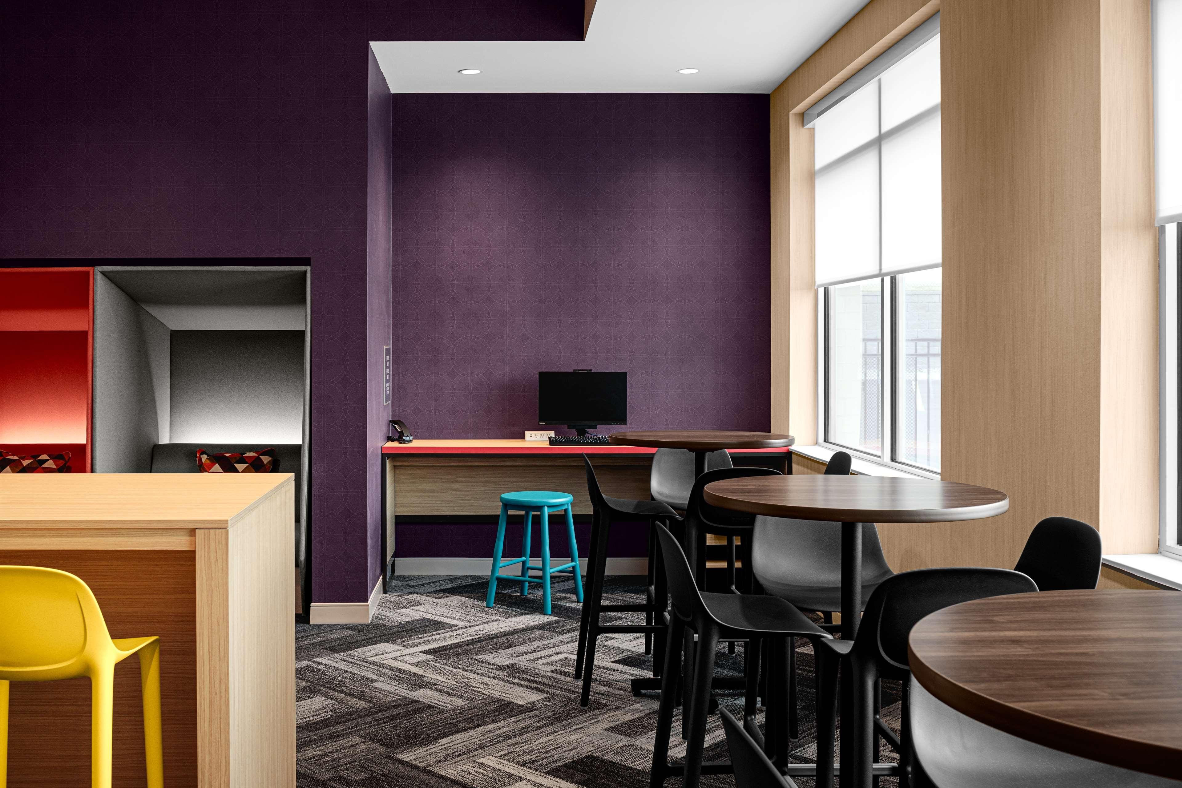 A modern interior with a purple accent wall, a wooden desk, a computer, and a seating area with chairs and a stool.