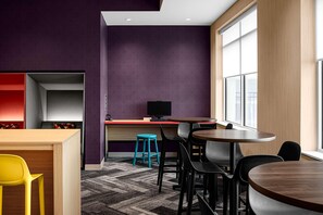 Un interior moderno con una pared de acento color púrpura, un escritorio de madera, una computadora y una zona de estar con sillas y un taburete.