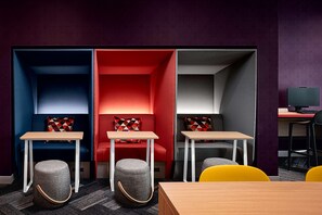 Um espaço de escritório moderno com três áreas de estar distintas, cada uma com um esquema de cores diferente (azul, vermelho e cinza), e uma mesa com um computador.