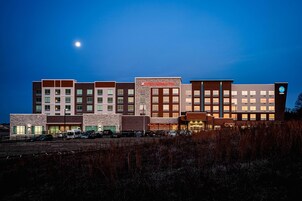 Un hotel de varios pisos con un diseño arquitectónico moderno, que presenta una combinación de fachadas de ladrillo y piedra, y un llamativo letrero de centro de jardinería.