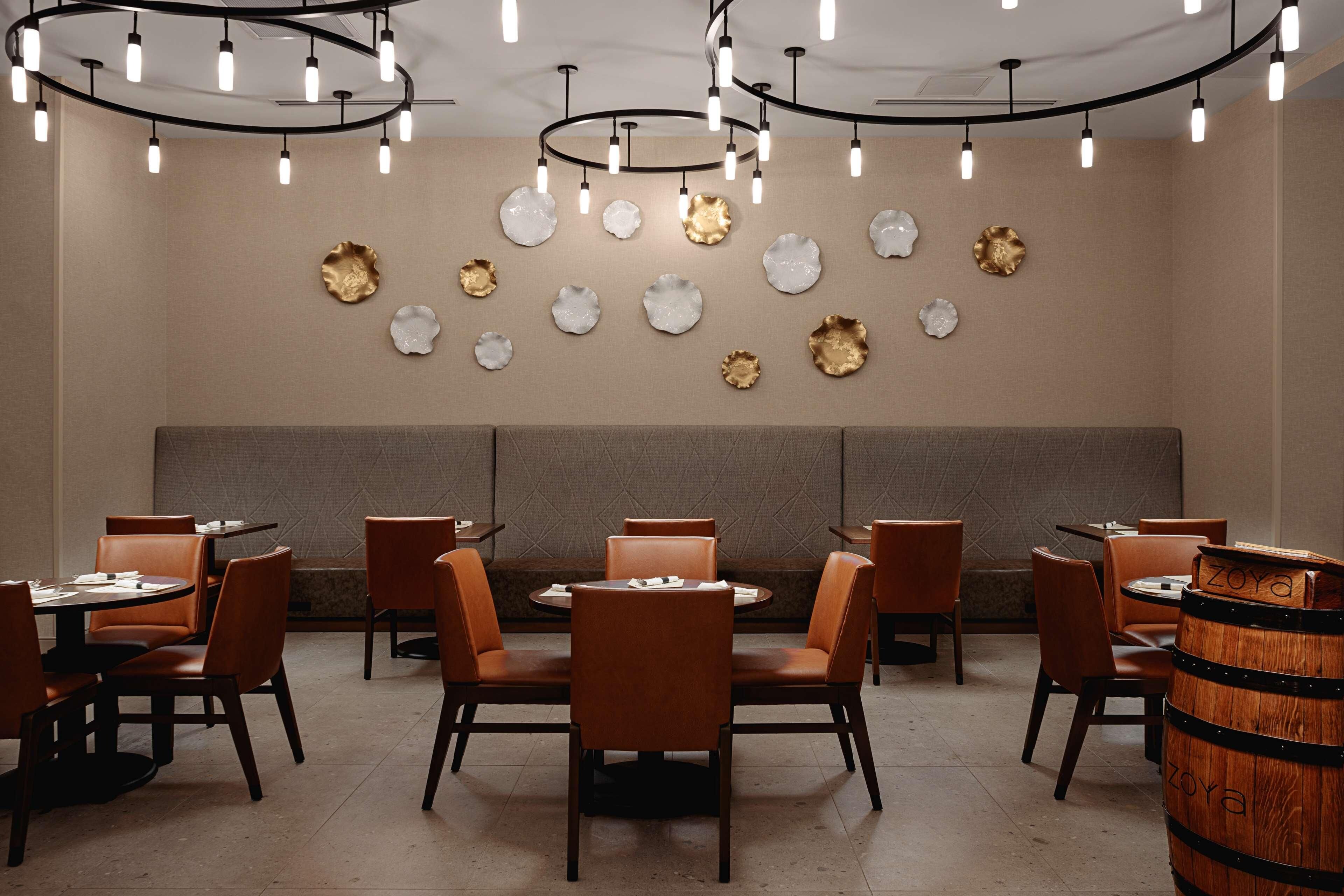 A restaurant interior with round tables, brown leather chairs, and a wooden barrel.