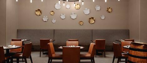 A restaurant interior with round tables, brown leather chairs, and a wooden barrel.