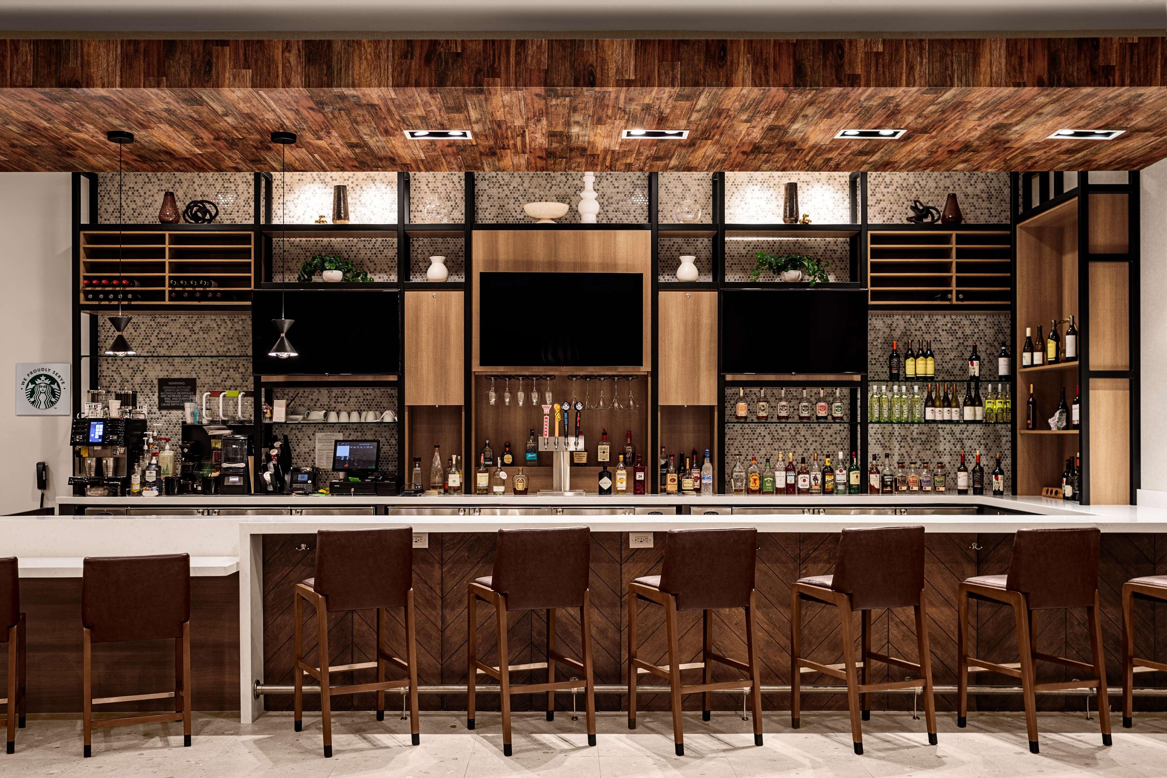 A modern bar with a wooden ceiling, a large TV screen, and a variety of liquor bottles.