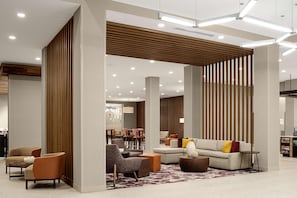 Un moderno hall de hotel con un sofá modular, sillones y una mesa de centro. Hay listones de madera en las paredes y una alfombra estampada en el suelo.