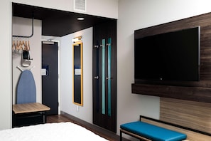 Ein Hotelzimmer mit einem Bett, einer Sitzbank, einem an der Wand montierten Fernseher, einem Spiegel und einer Tür mit türkisfarbenen Griffen.
