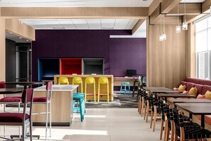 Uma área de refeições moderna com várias mesas e cadeiras, um espaço de bar central e uma área de estar com sofá.
