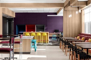 Un comedor moderno con varias mesas y sillas, una zona de bar central, y un área de estar con un sofá.